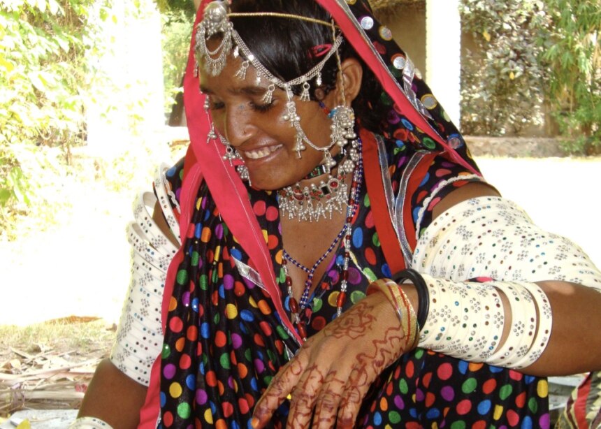 Rabari woman relaxes wearing ivory armbands and silver necklaces.
