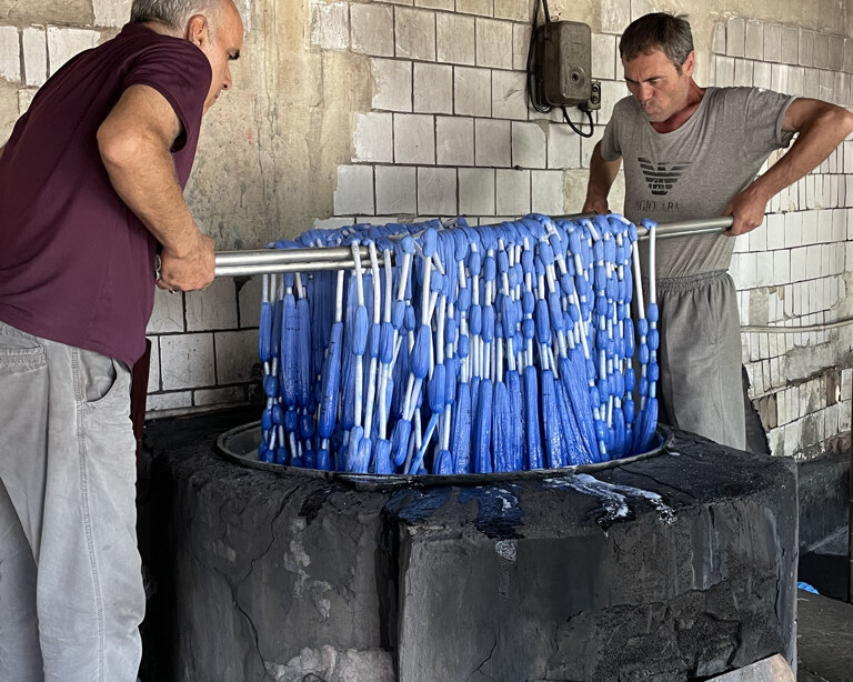 Two workers dip tied ikat warp threads into blue dye.