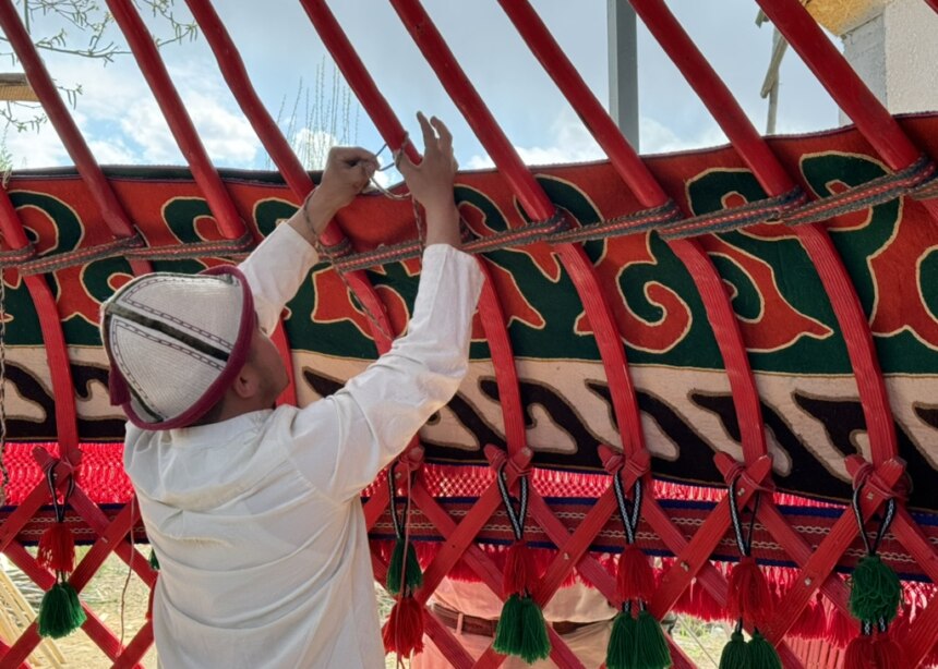 Man in a traditional Kyrgyz nomad hat ties yurt sections; Naryn, Kyrgyzstan.