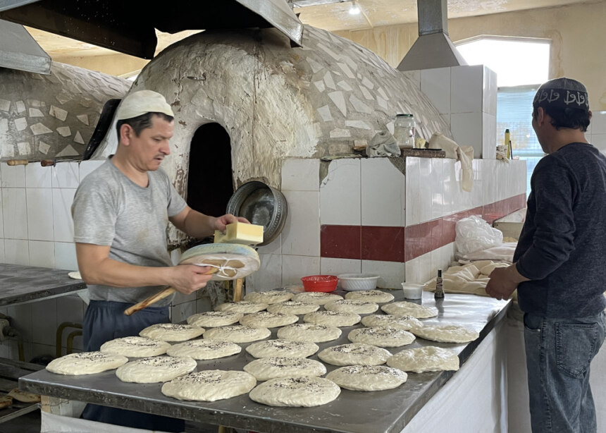 Baker standing in front of round tandoor bread oven, preparing raw dough disks for baking.