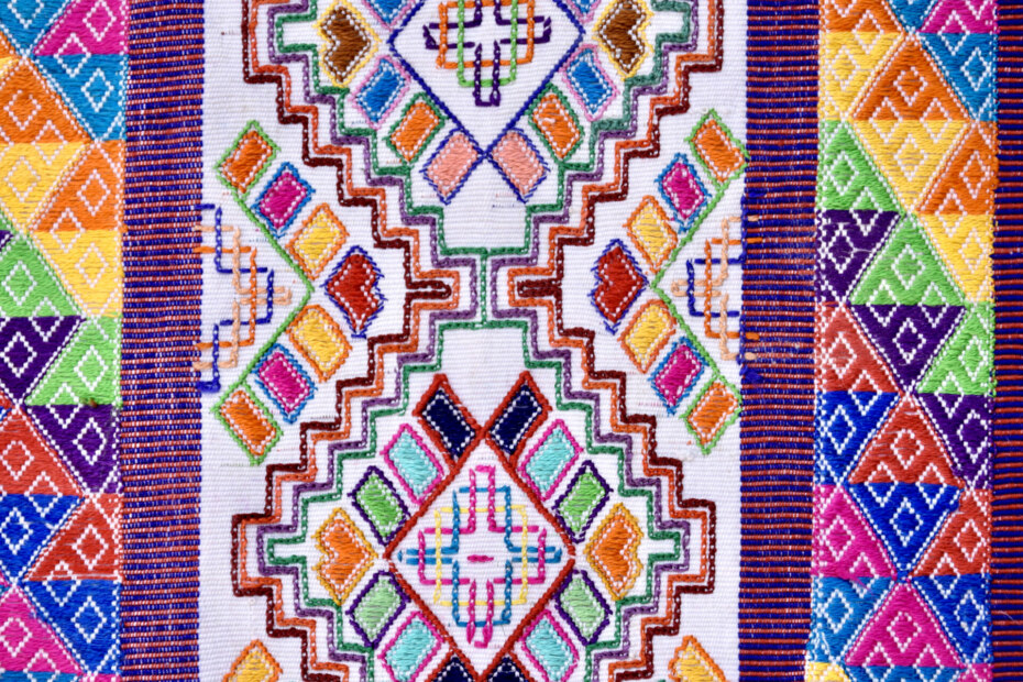 Handwoven white cotton weaving with brightly colored geometric patterns.