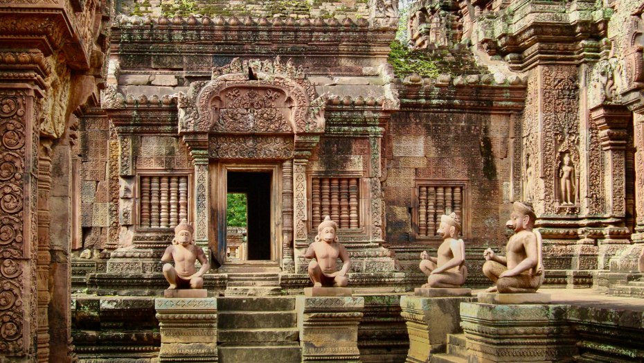 Four stone sculptures of Hanuman monkey gods surround a stone carved temple at Angkor Park.