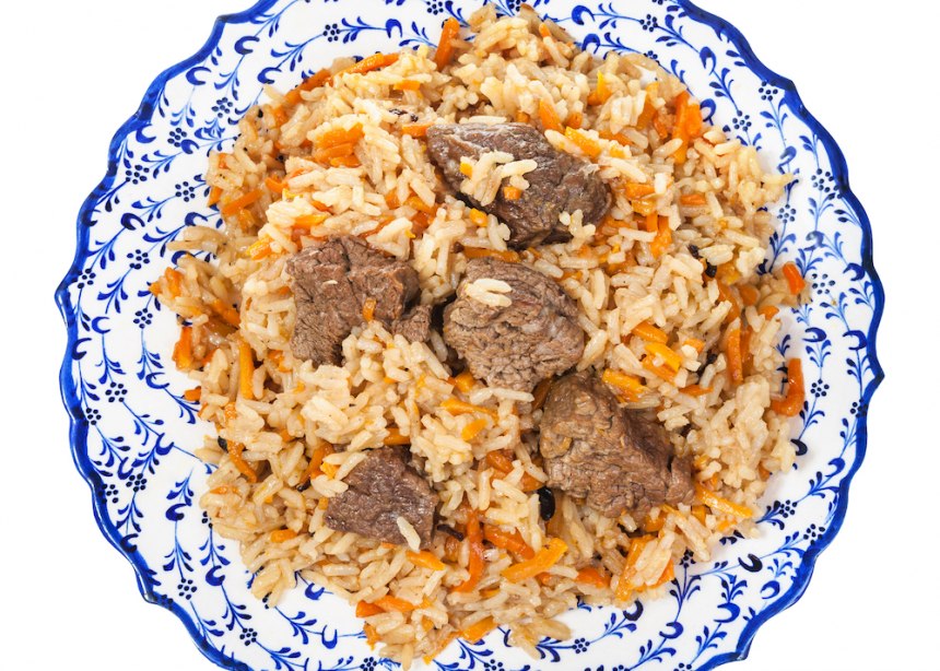 Blue and white plate full of rice and meat dish called Plov.