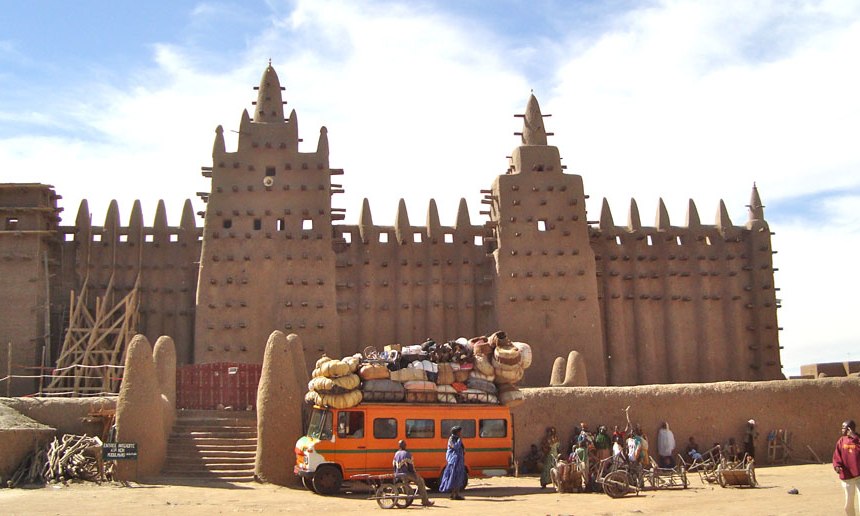 Enormous adobe block mosque with two towers and a bus in front.