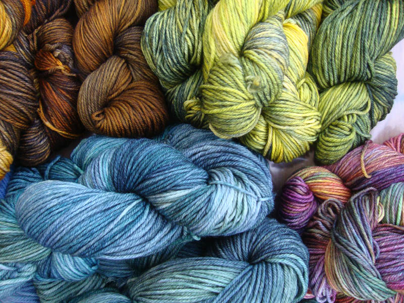 Pile of hand-dyed yarns in blue and green hues.