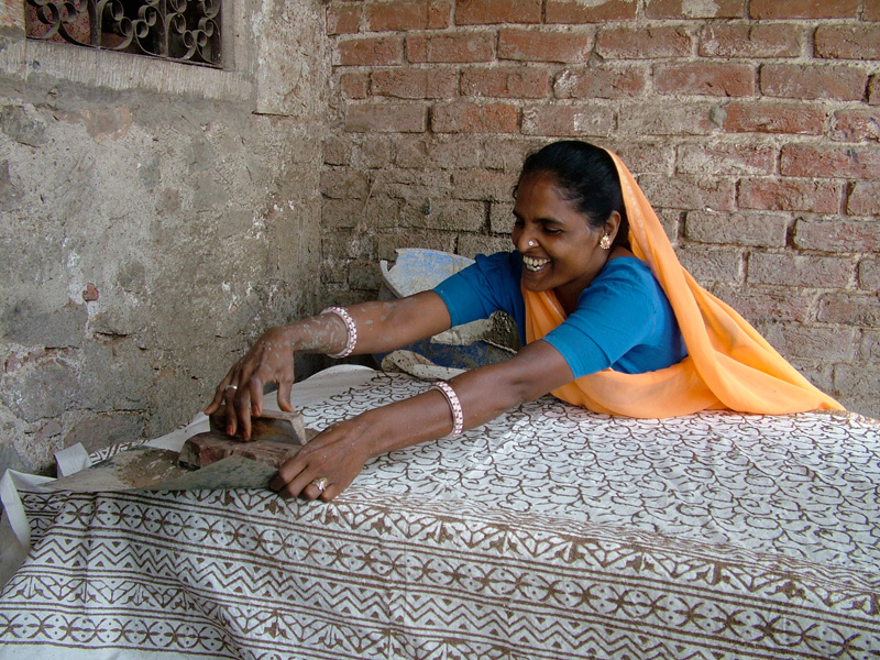 Woman leans over cloth to stamp the far edge; INDIA