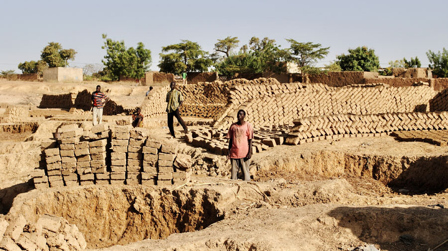 Three men stand by piles of handmade adobe bricks; Mali..