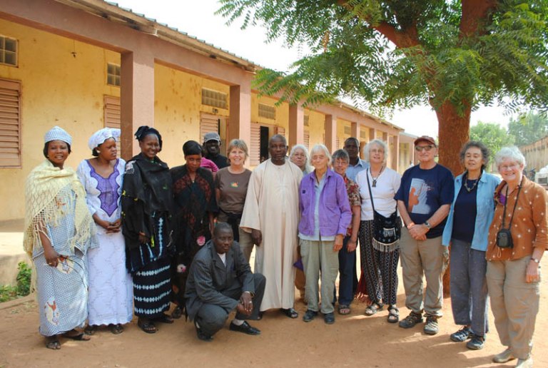 Staff of Segou school and BTSA travelers pose next to the classrooms in the bare schoolyard.