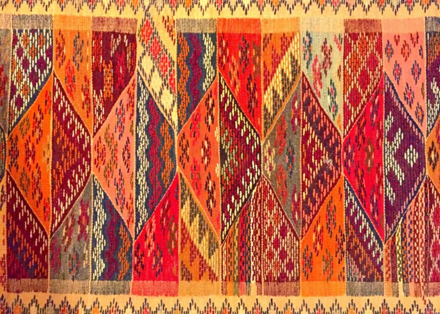 Hand-woven woolen rug in 'sunset' colors of reds, oranges, yellow and gold.