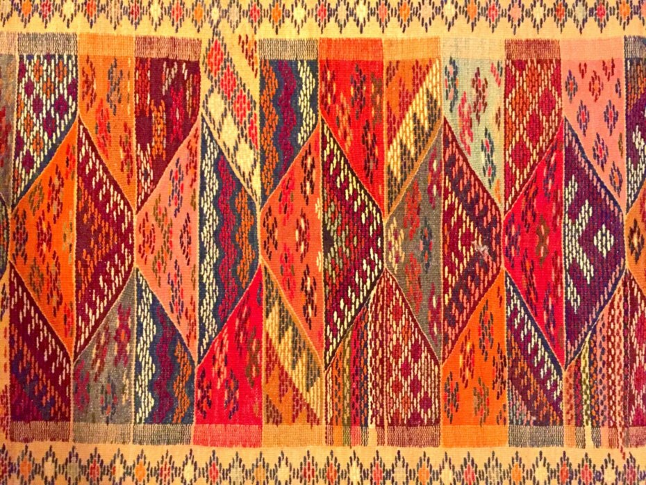 Hand-woven woolen rug in 'sunset' colors of reds, oranges, yellow and gold.
