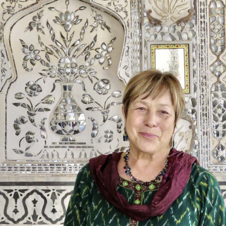 Smiling woman stands in front of a decorative mirrored wall in a palace in India.