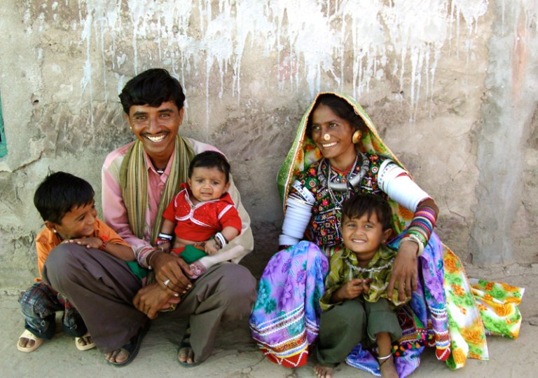 A family dressed in bright garments relaxes in the shade.