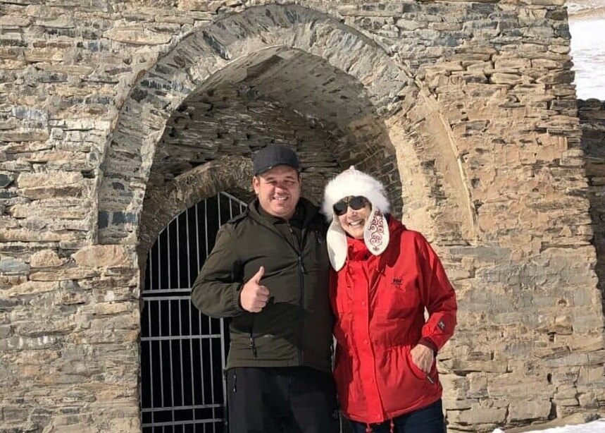 Two smiling people stand at the entrance to the Tash-Rabat caravanserai in Kyrgyzstan.