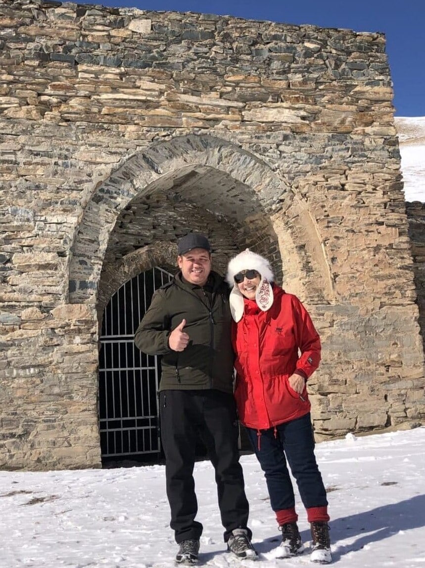 Two smiling people stand at the entrance to the Tash-Rabat caravanserai in Kyrgyzstan.