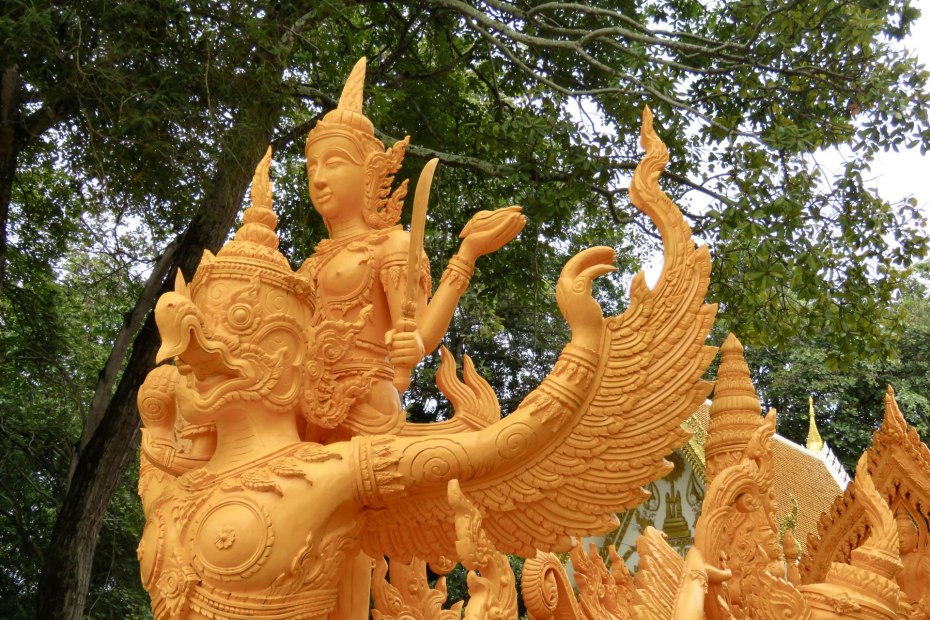 Golden yellow colored sculpture of a huge Garuda bird/god with hooked beak and human arms combined with wings.