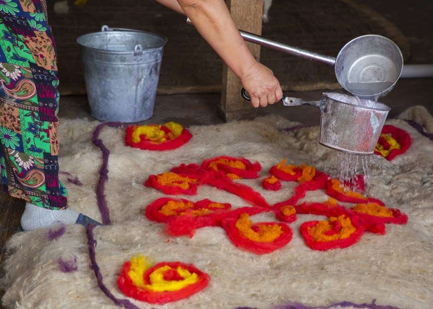 A woman lays red and yellow felt roving on top of a felted backing.