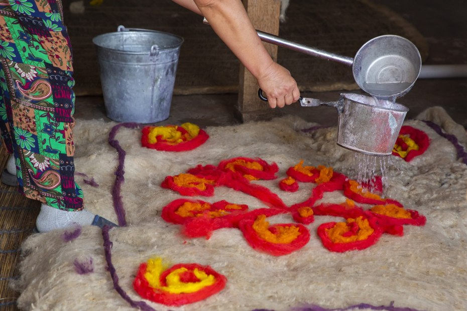 A woman lays red and yellow felt roving on top of a felted backing.