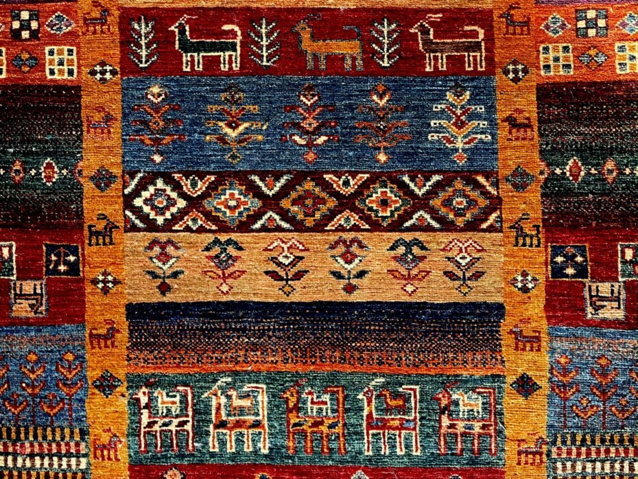 Section of a handmade carpet in oranges and blues with animal designs.