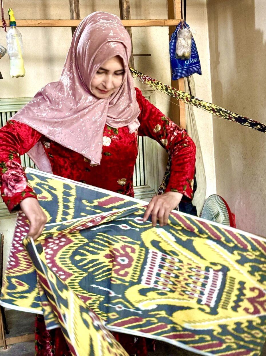 Ikat hand weaver in Margilan, Uzbekistan, folds up her bright yellow/black/red work