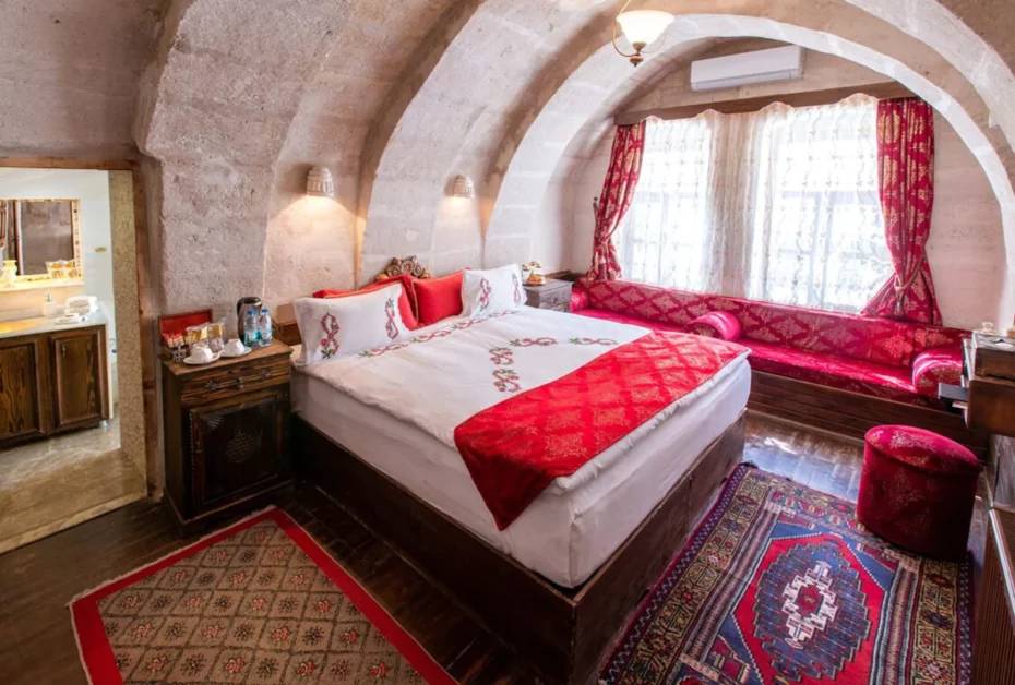 Hotel room cut out of the tufa rock, with double bed and red spread.